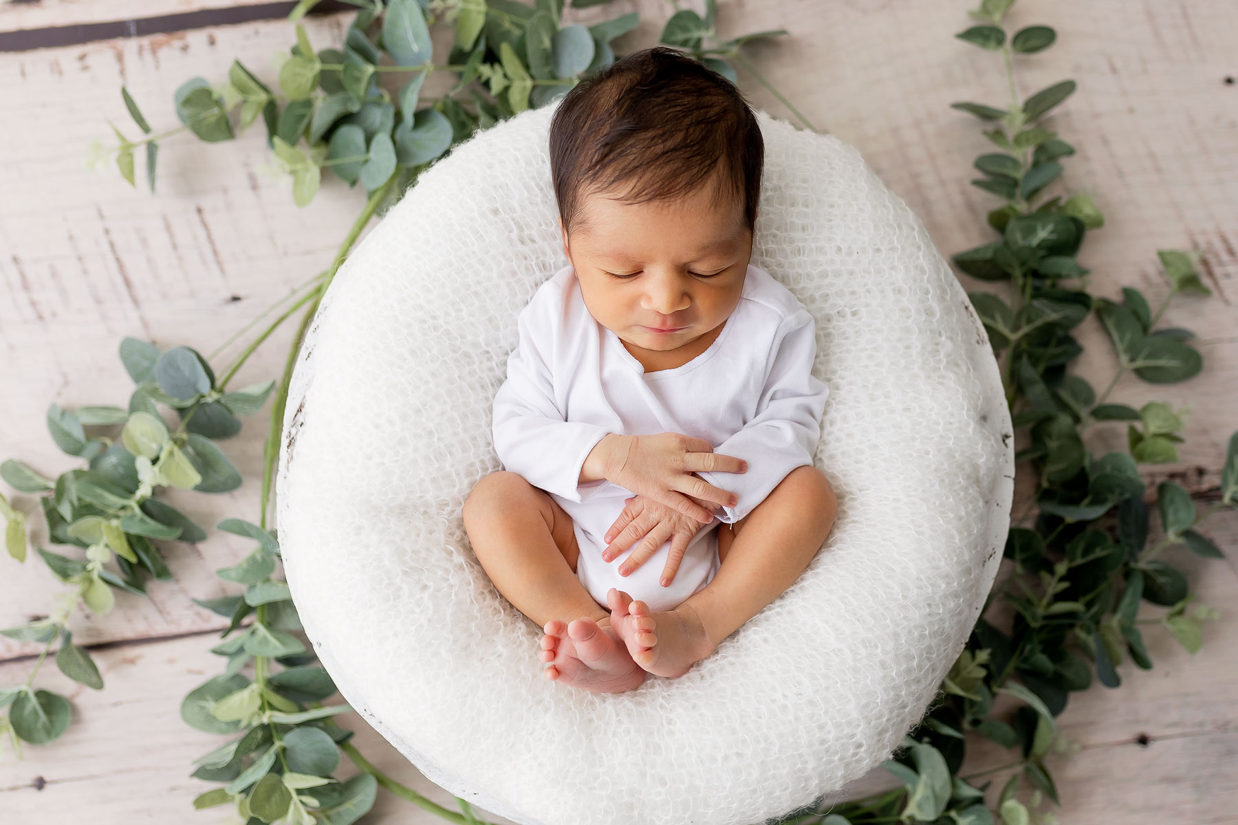 newborn in white nest surrounded by greenery.